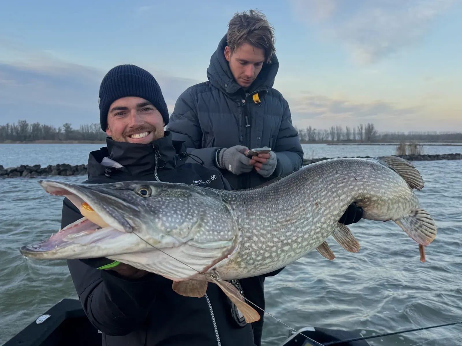 De snoek gaat op de foto voor ze terug het water in gaat, met een stenen dam op de achtergrond