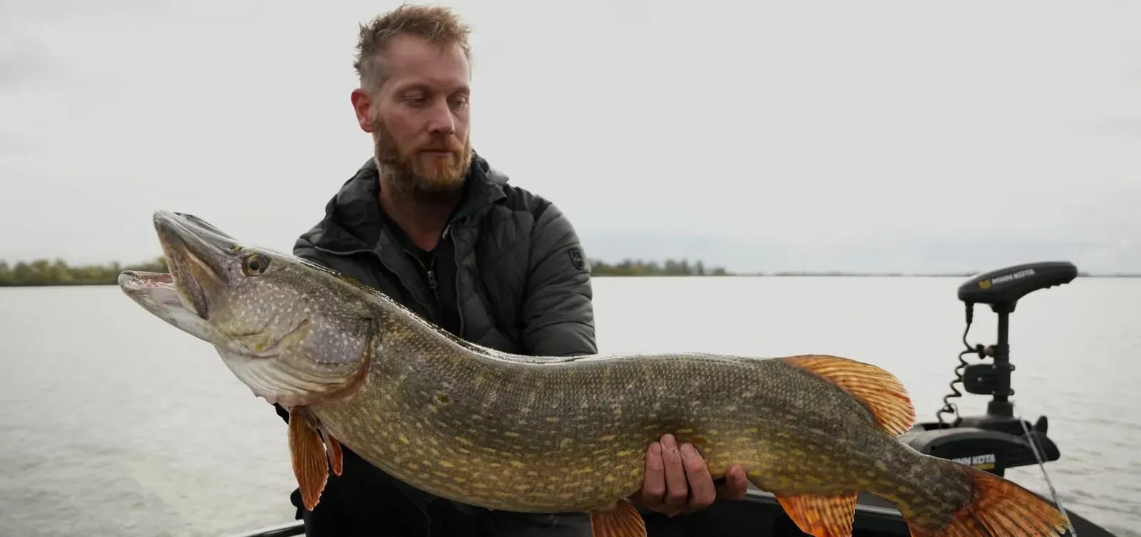 Jasper met dezelfde snoek op het dek van de boot, met het water erachter