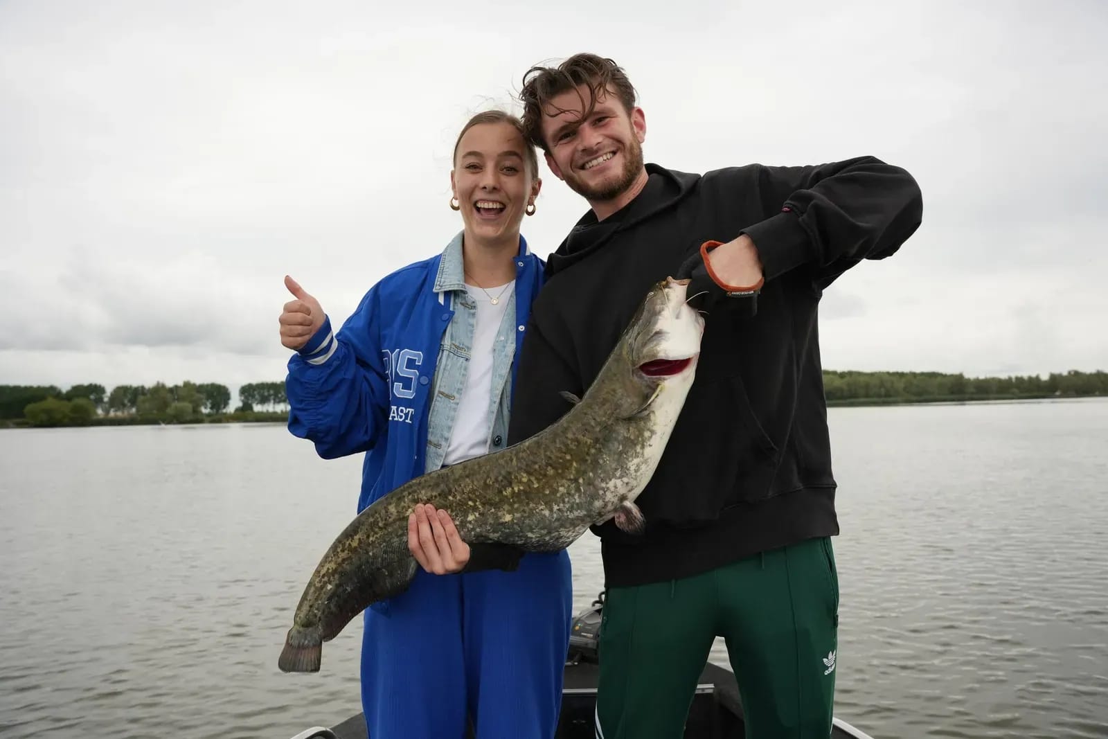 Lexi en Mike met de meerval die op licht materiaal werd gevangen, duim omhoog