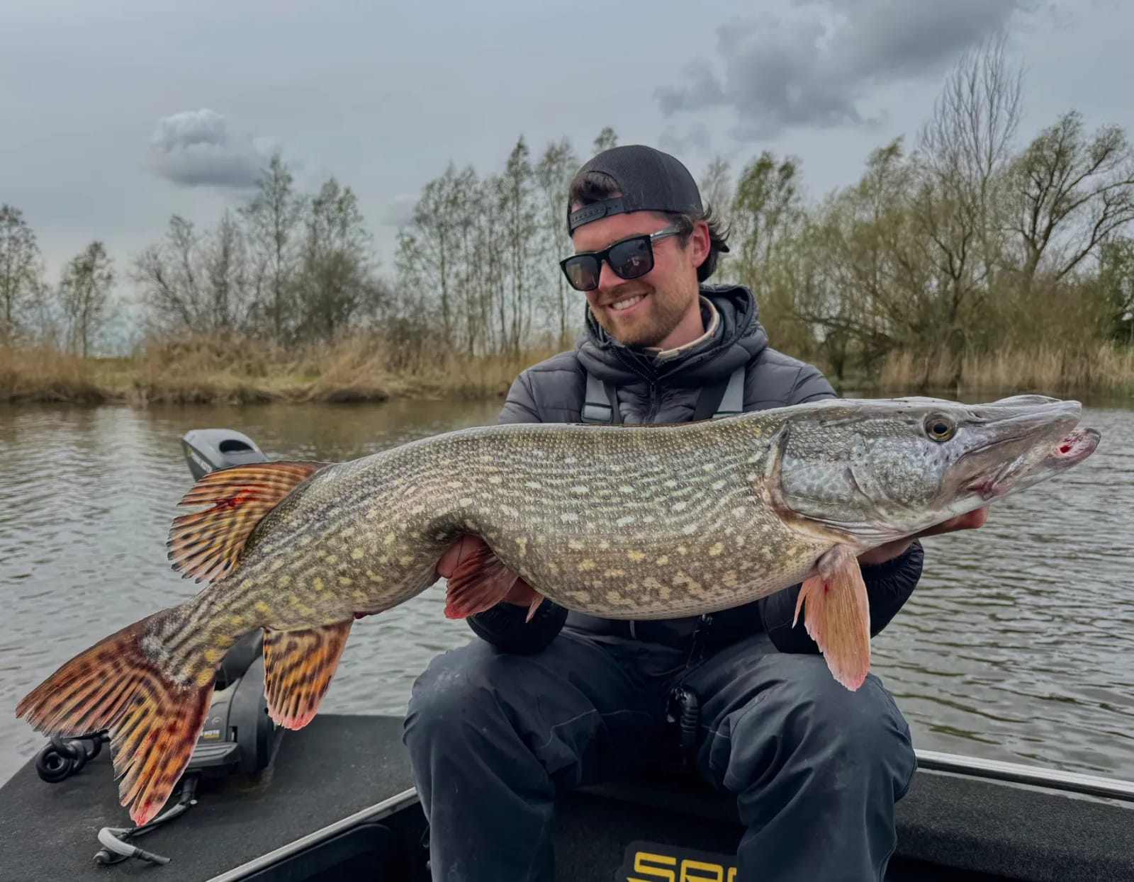 Luc met een snoek langs een rivieroever in het voorjaar