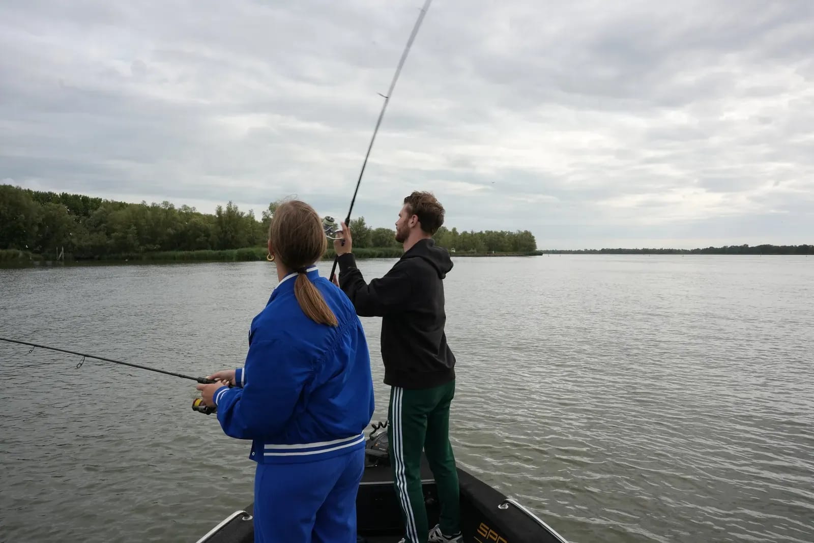 Lexi en Mike vissen naast elkaar vanaf de boot, met de rietkraag op de achtergrond