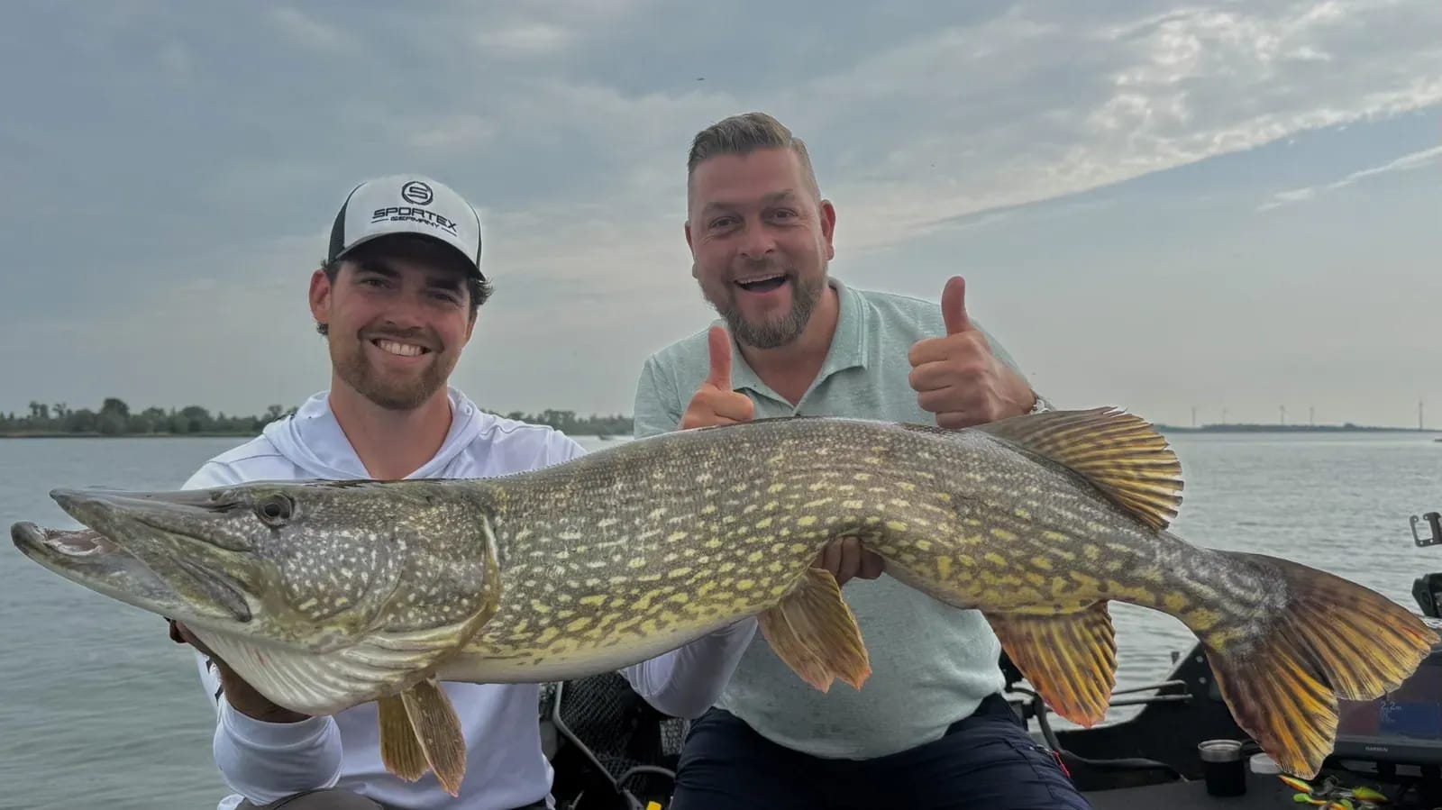 Twee mannen houden samen de snoek van 116 centimeter vast, een van hen steekt zijn duim omhoog