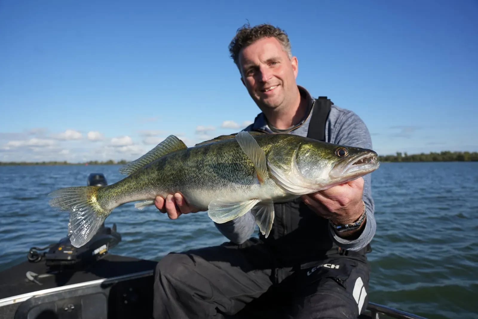 Mark met de snoekbaars van 75 centimeter, met een blauwe lucht boven de rivier