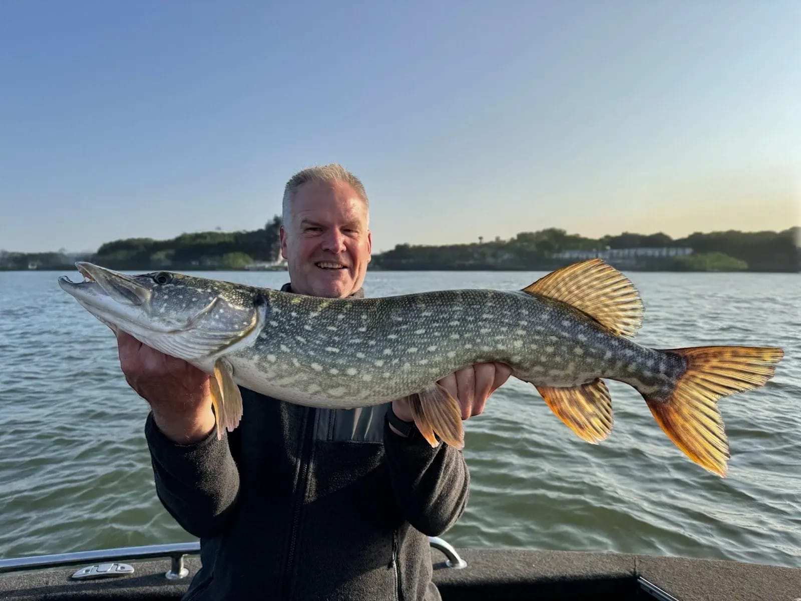 Koos houdt zijn snoek over de volle breedte vast, met de zon laag boven het water