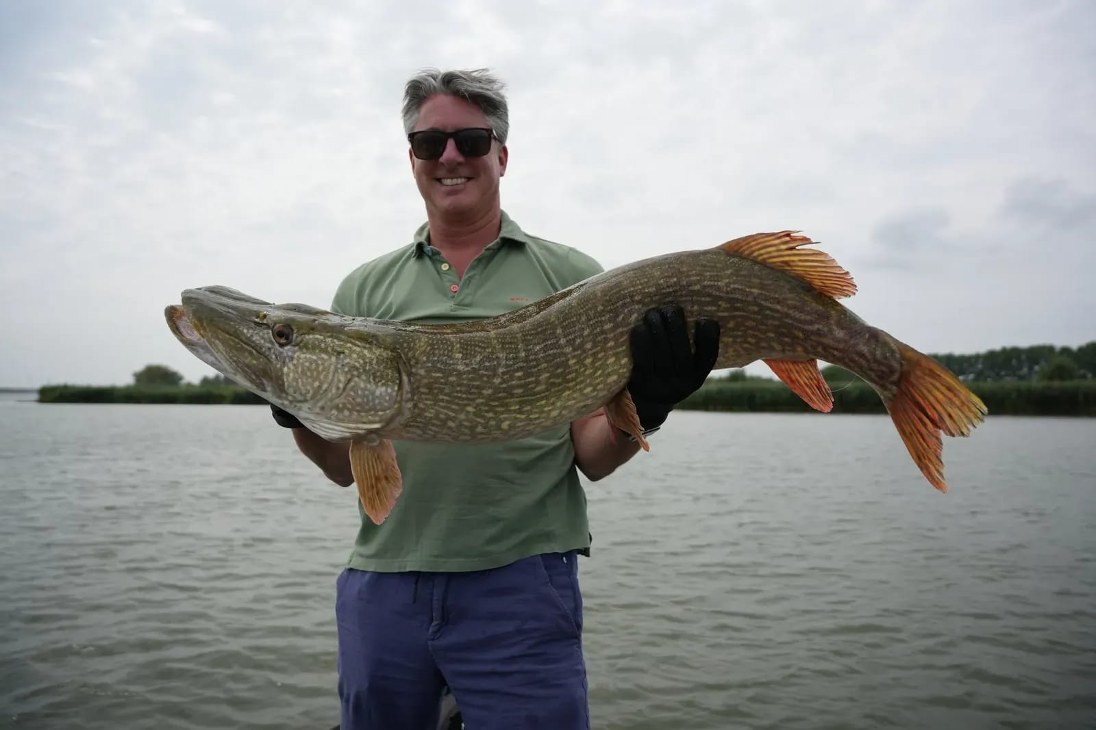 Een gast houdt de snoek van 115 centimeter over de volle breedte van het beeld vast