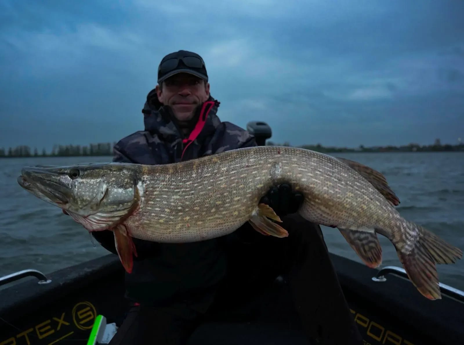 Dezelfde snoek in het blauwe uur, met de buitenboordmotor op de achtergrond
