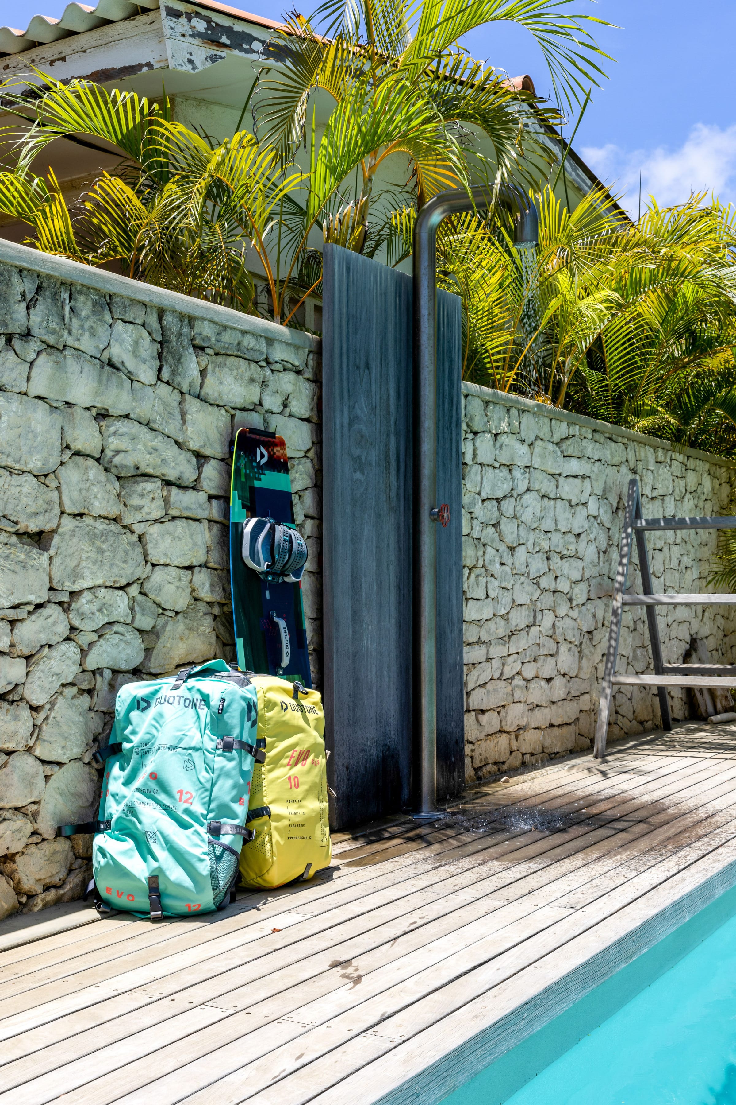 Douche extérieure près de la piscine, entourée de pierre naturelle et de palmiers