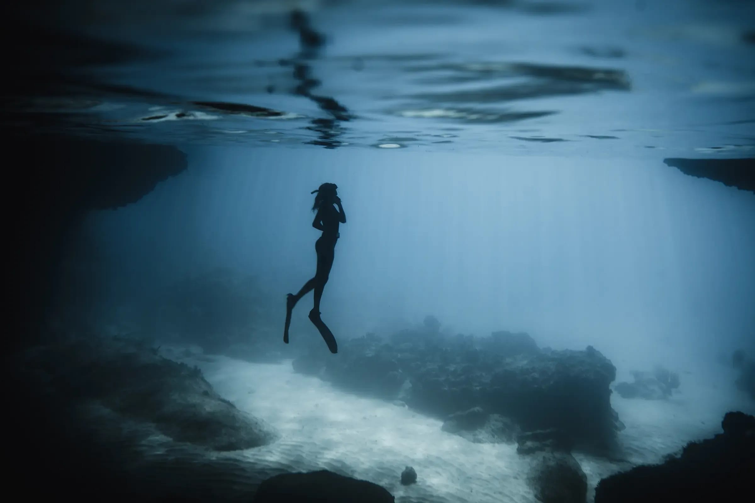 Ein Freitaucher als Silhouette unter Wasser vor Curaçao